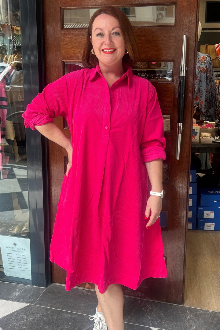 Woman in a bright pink dress standing in front of a store entrance.
