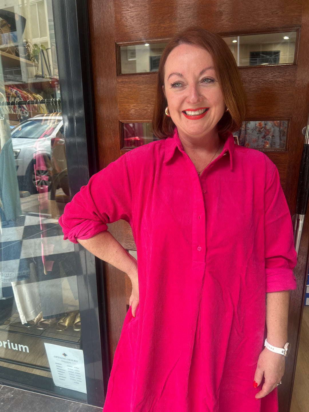 Woman in a bright pink shirt standing in front of a store entrance.