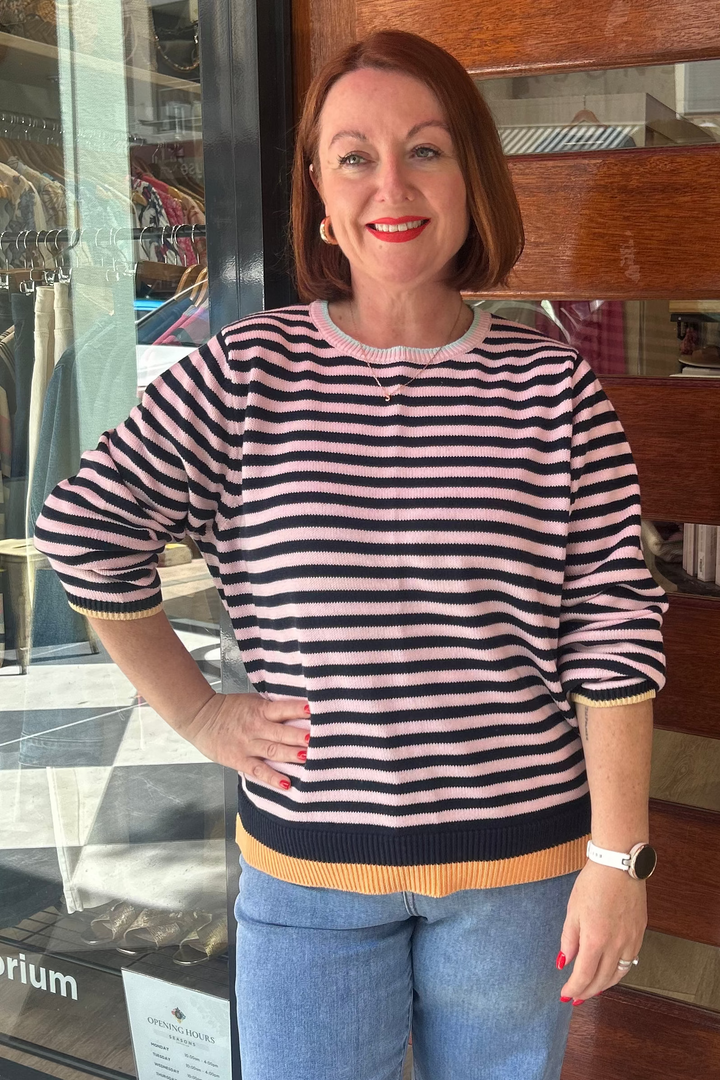 Woman standing in front of a store entrance with a striped shirt and jeans.