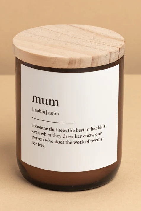 A candle jar with a wooden lid labeled 'mum' with a definition of the word 'mum' written on it. The candle appears to be made of a creamy white wax and is set against a neutral background.