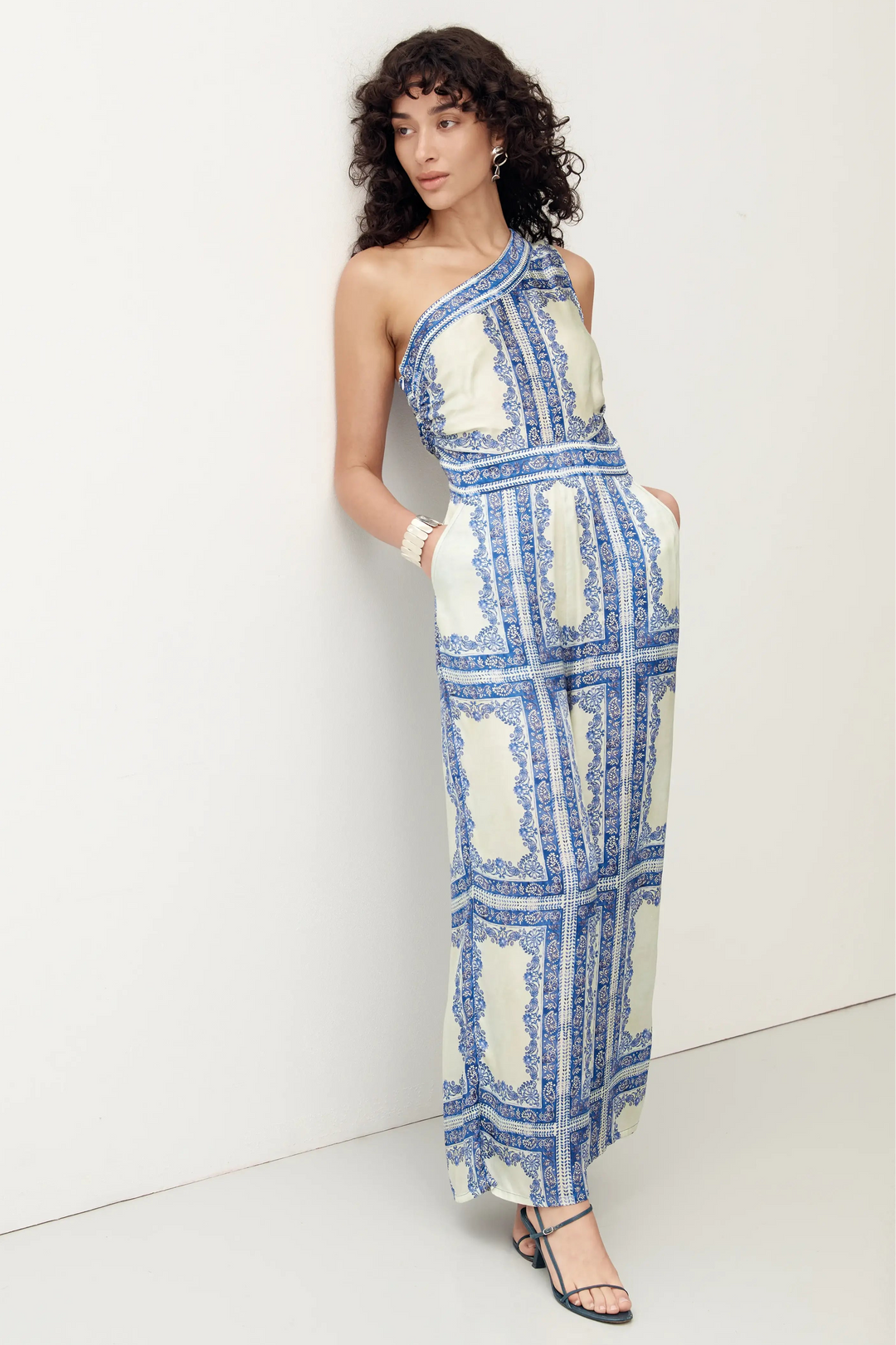 Woman wearing a blue and green patterned one-shoulder dress against a white background