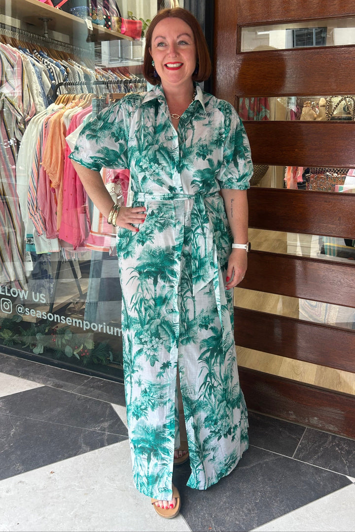 Woman in a green floral dress standing in front of a store entrance.