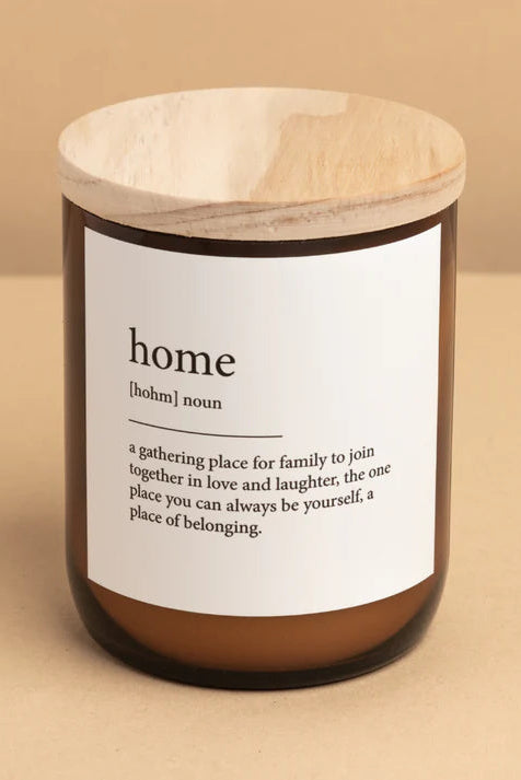 A candle jar with a wooden lid labeled 'home' containing a white candle, on a neutral background.