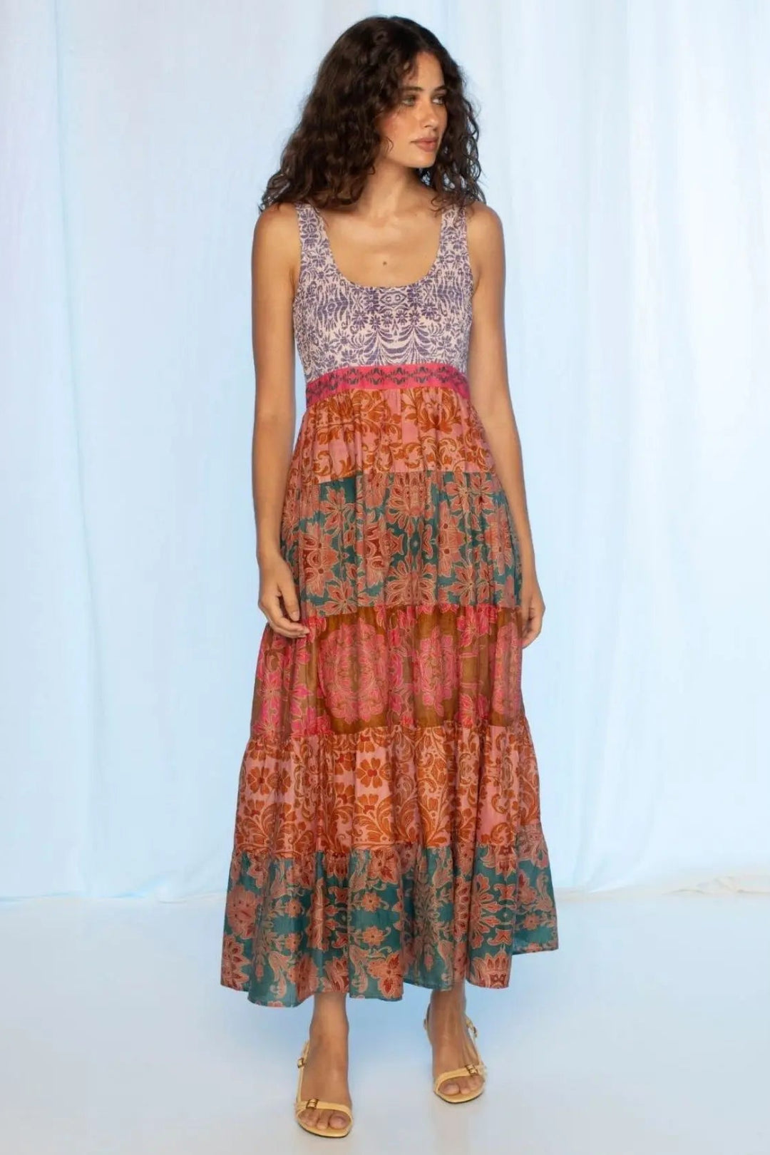 Woman wearing a layered dress with a patterned top and floral skirt against a light blue curtain background.