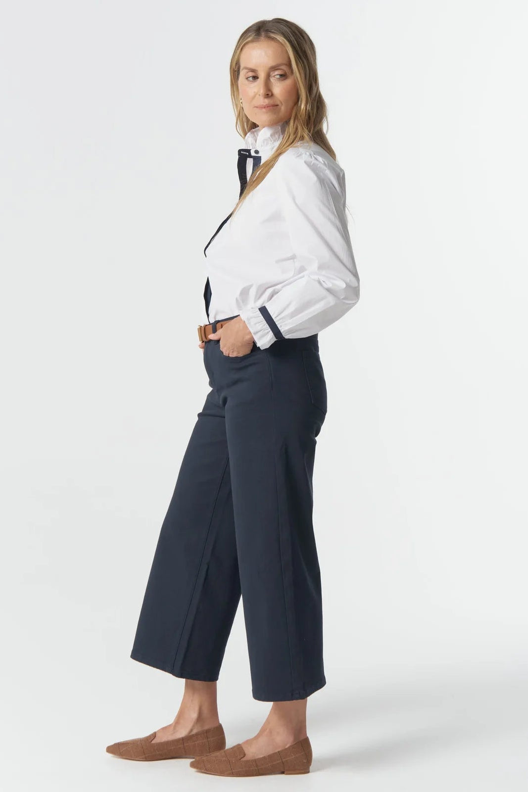 Woman wearing a white shirt, navy pants, and brown shoes on a white background