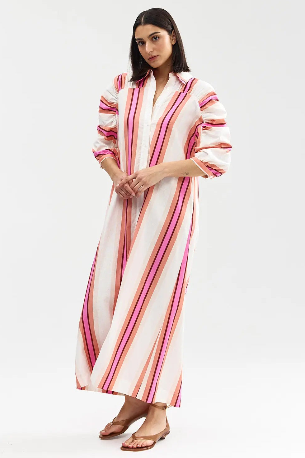Woman wearing a long, striped dress with pink and orange stripes on a white background