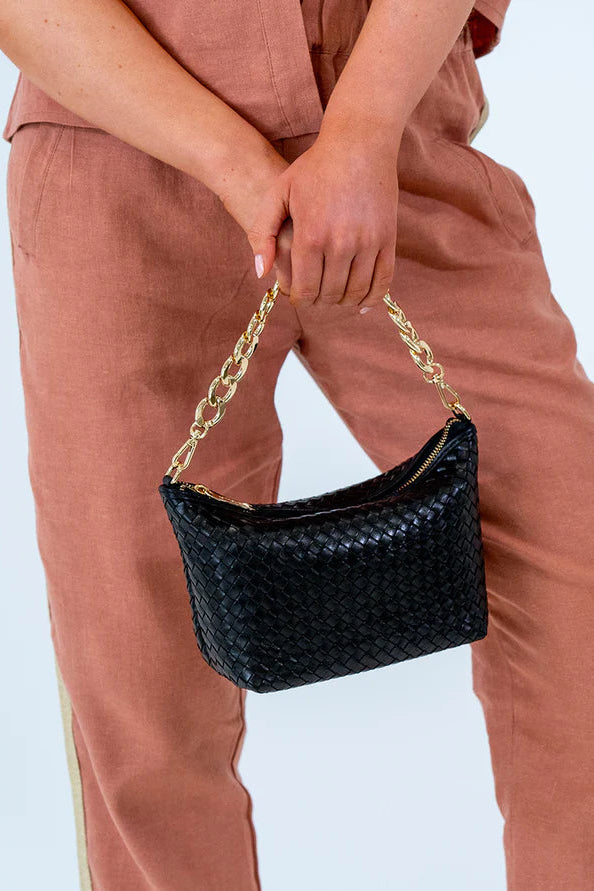 A person holding a black intrecciato-style leather handbag with a chain shoulder strap and gold hardware.
