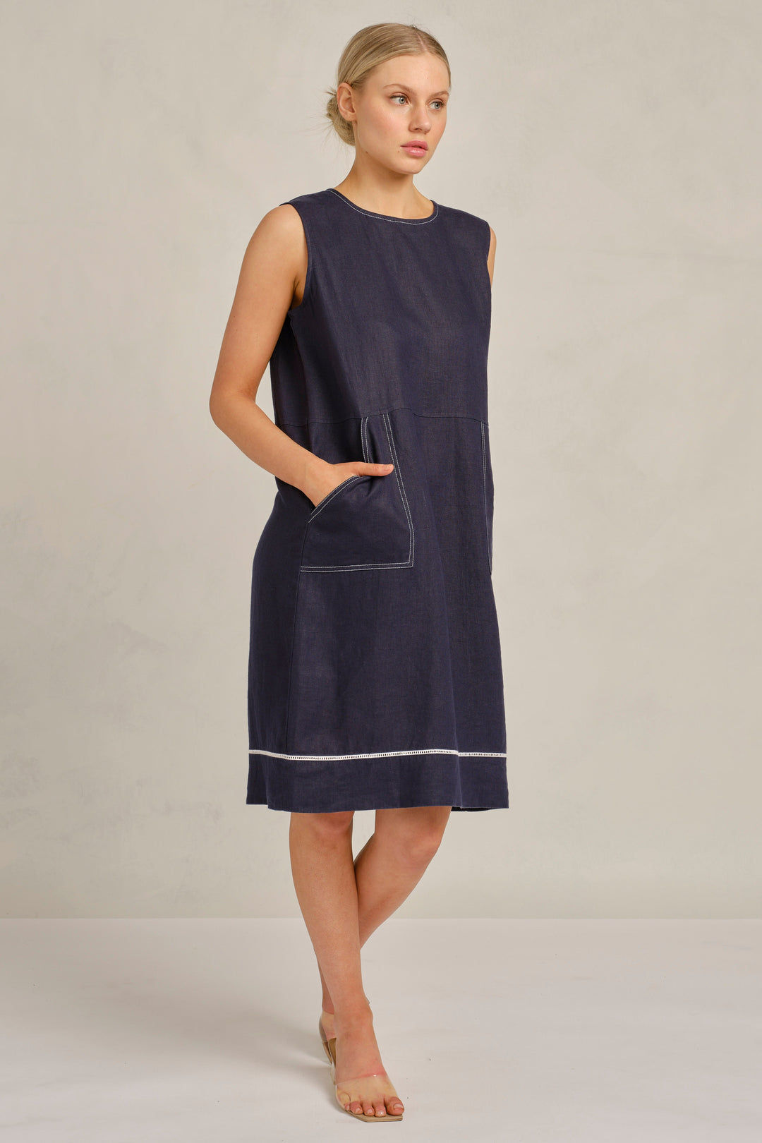 Woman wearing a navy sleeveless dress with a pocket on a beige background