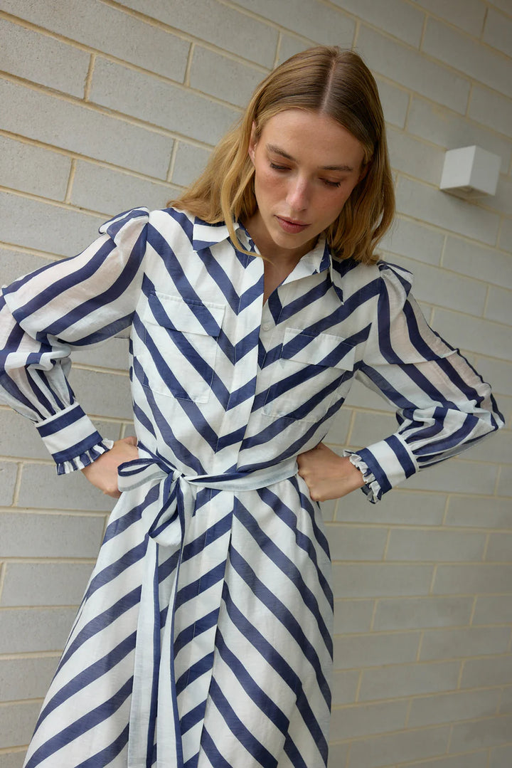 Woman wearing a blue and white striped dress against a light brick wall.