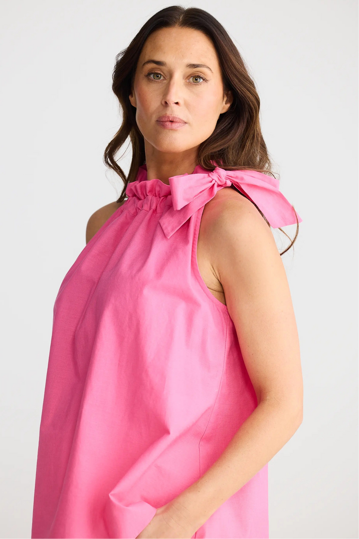 Woman wearing a pink dress with a bow detail on a white background