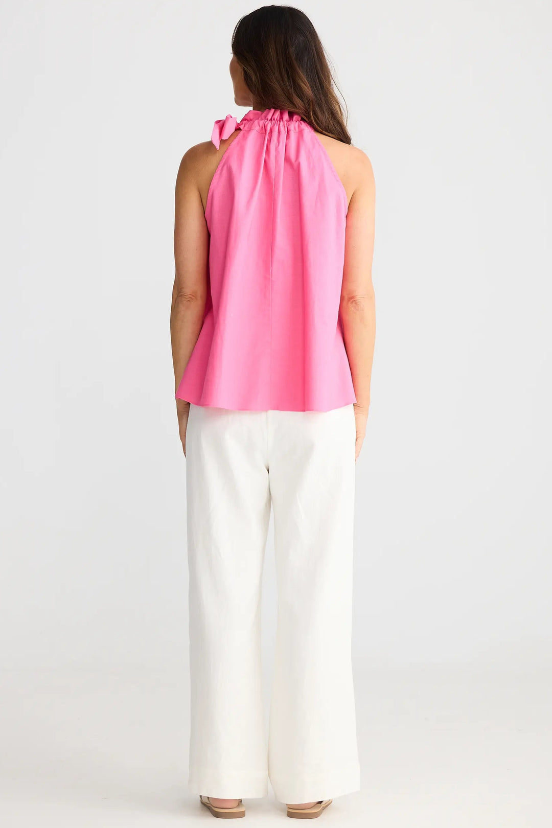 Woman wearing a pink sleeveless top and white pants on a plain background