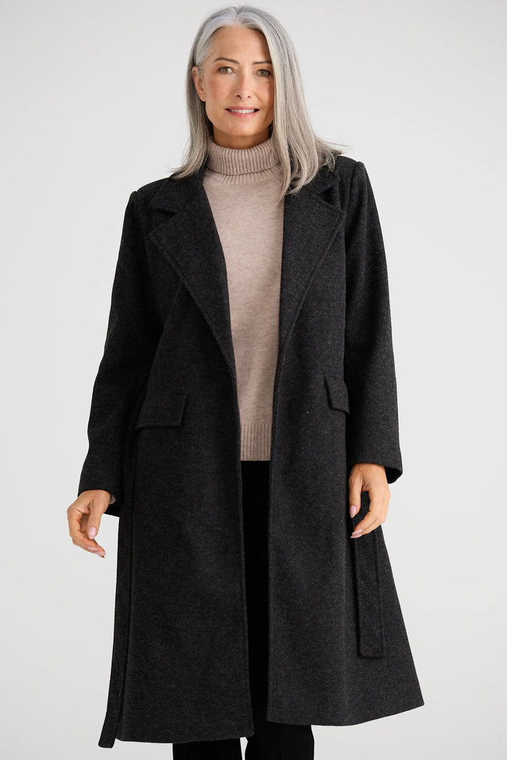 Woman wearing a long black coat over a beige sweater on a white background