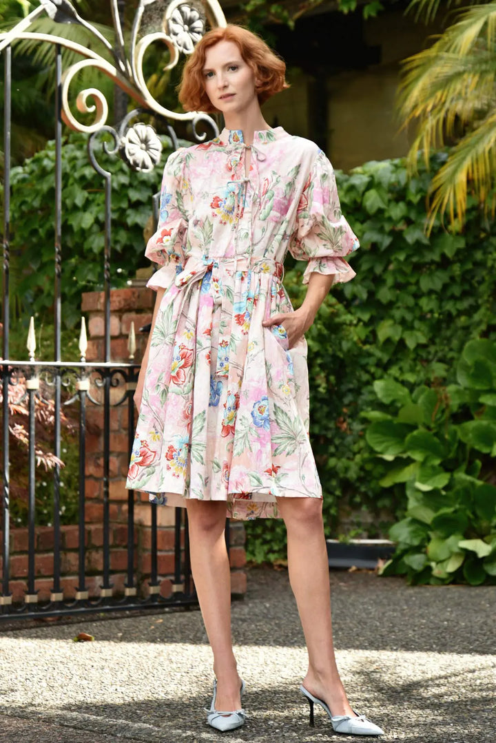 Woman wearing a floral dress standing in front of a decorative metal gate and greenery.