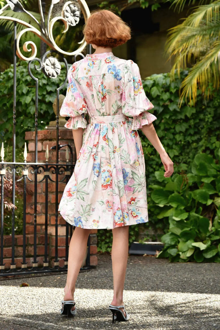 Woman in a floral dress walking outdoors with greenery and a gate in the background