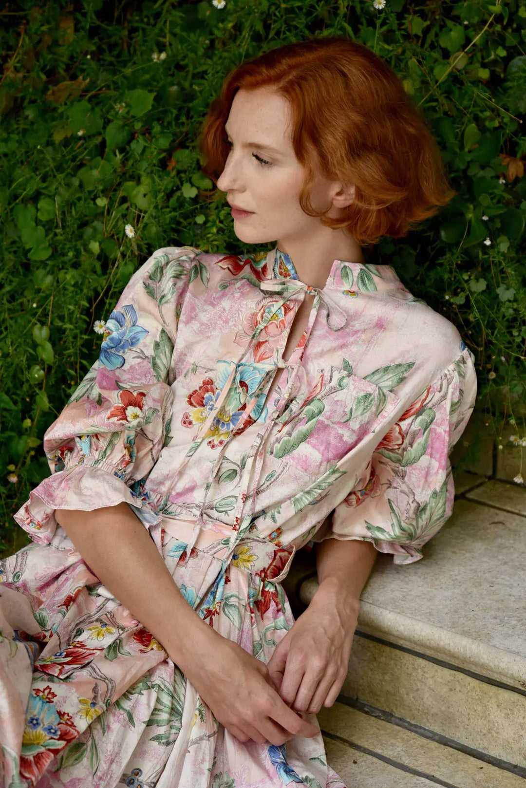Woman in a floral dress sitting outdoors with greenery in the background