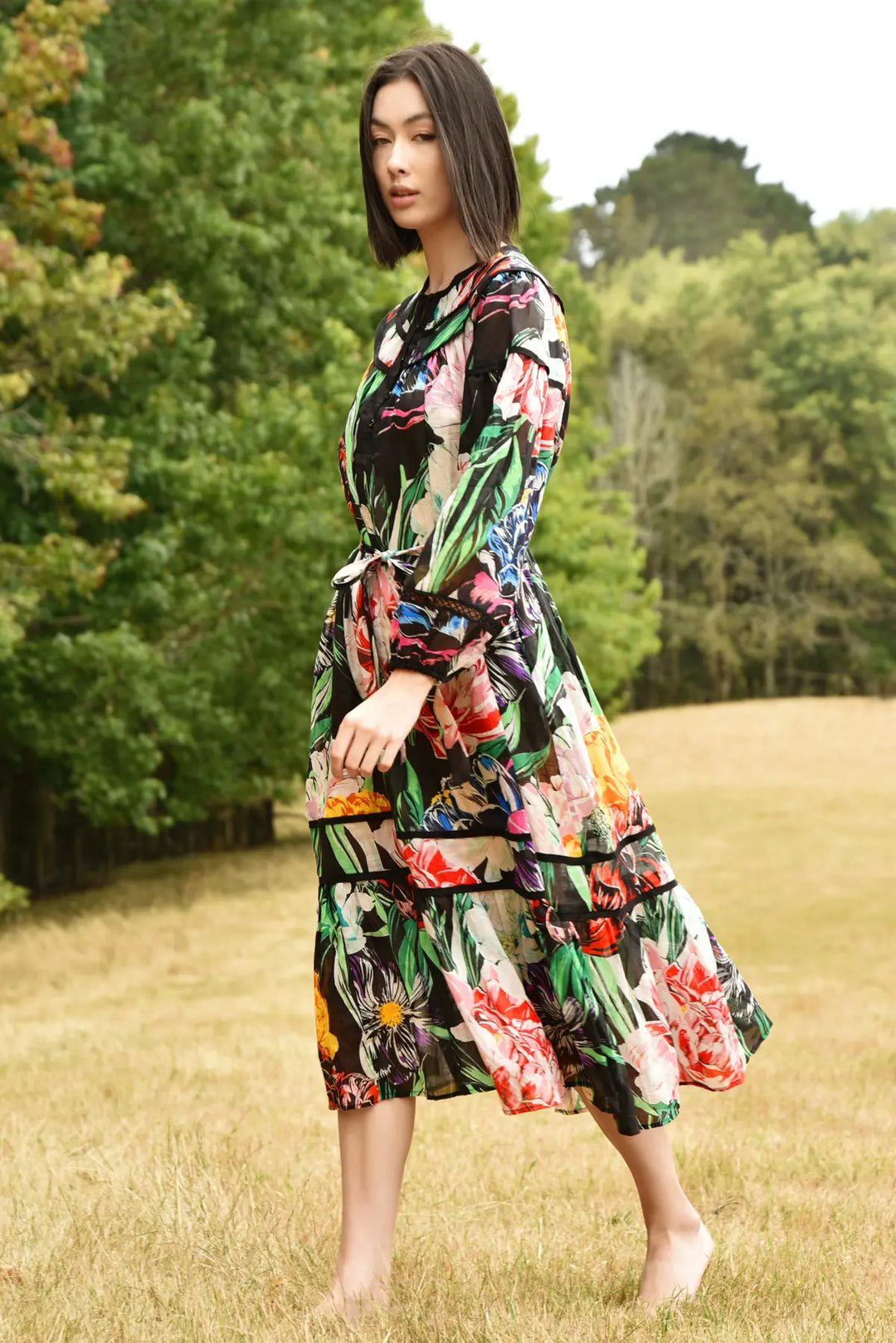 Woman in a colorful floral dress standing in a grassy field with trees in the background