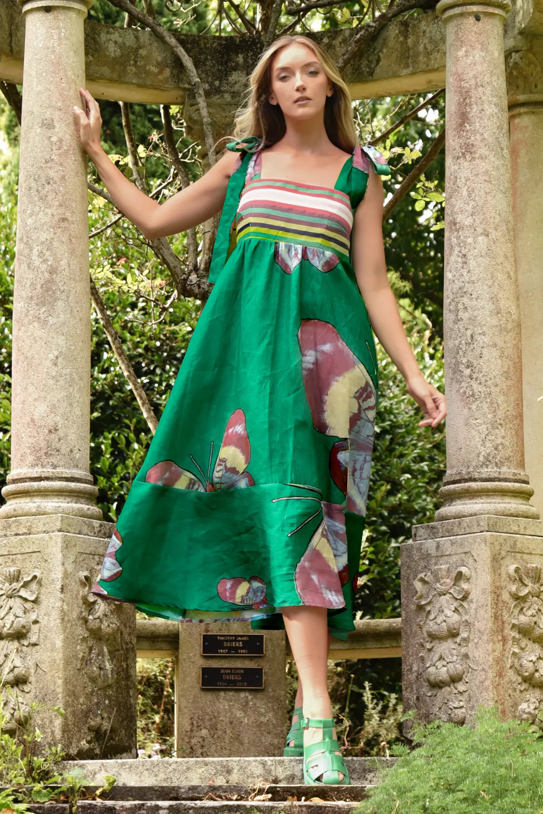 Woman in a green dress with floral patterns standing in a garden setting.