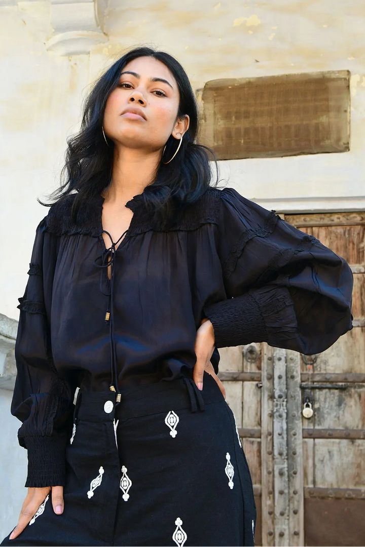 A woman wearing a black Luna Blouse with unique textural applique trims and antique bronze tassels.