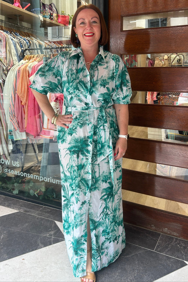 Woman in a green and white patterned dress standing in front of a store with clothing racks.