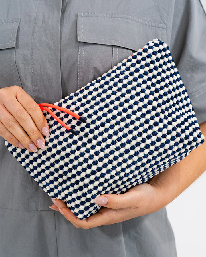 Person holding a navy and white patterned clutch with orange handle. Elms & King Napili Large Navy White