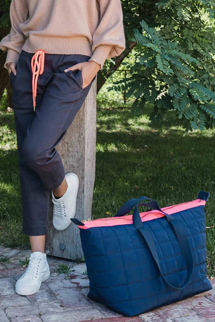 Person standing next to a navy blue tote bag with pink interior on a paved path.