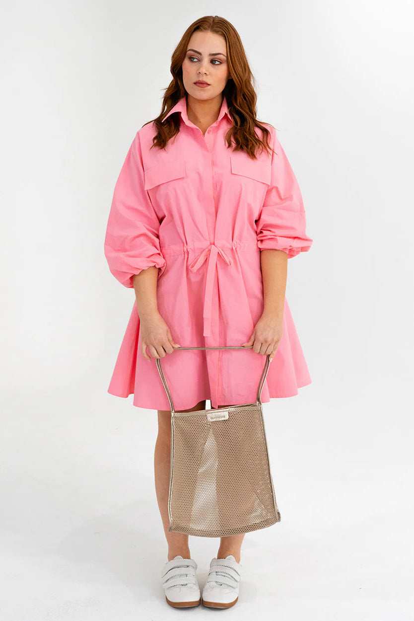 Woman wearing a pink dress holding a beige bag on a white background