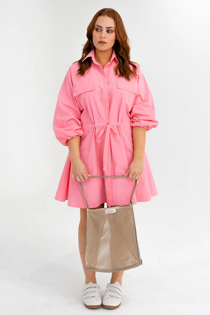 Woman wearing a pink dress holding a beige bag on a white background