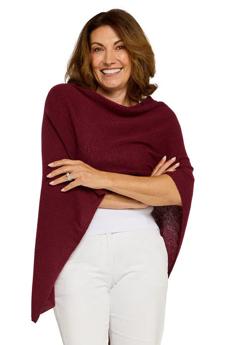 Woman wearing a burgundy poncho over a white top and pants on a white background