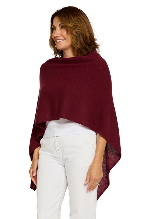Woman wearing a burgundy poncho and white pants on a white background