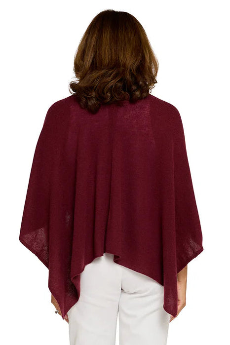 Woman wearing a burgundy poncho and white pants on a white background