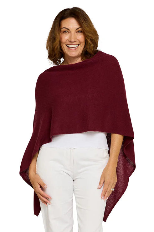 Woman wearing a burgundy poncho and white pants on a white background