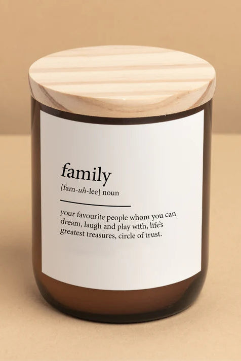 A soy candle in a clear jar with a wooden lid, labeled 'family' with a definition next to a beige background.