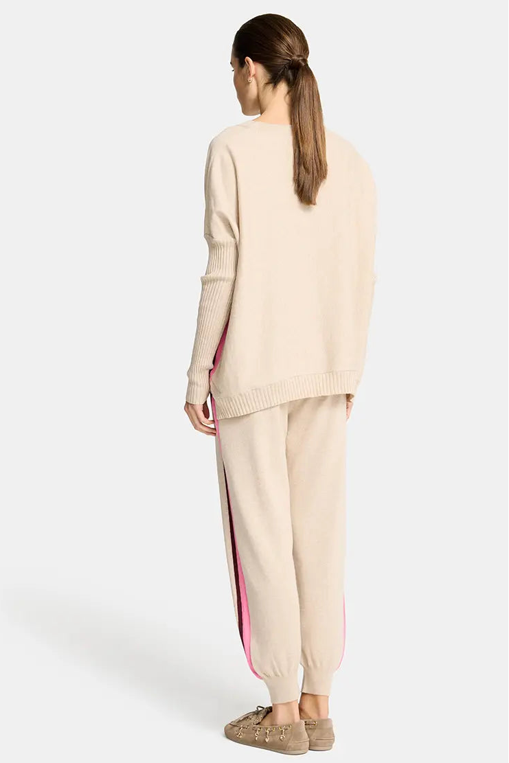 Woman wearing a beige sweater and pants with a pink stripe on a white background