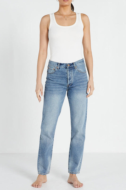A female model wearing a white tank top and mid blue slim mum jeans with a straight leg cut.