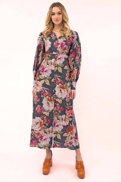 A model wearing a floral maxi dress with a shirt-style collar and long sleeves, in a mix of dark and light colors.