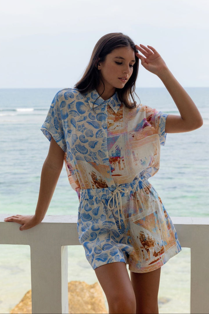Woman in a patterned outfit standing by a railing with an ocean view.