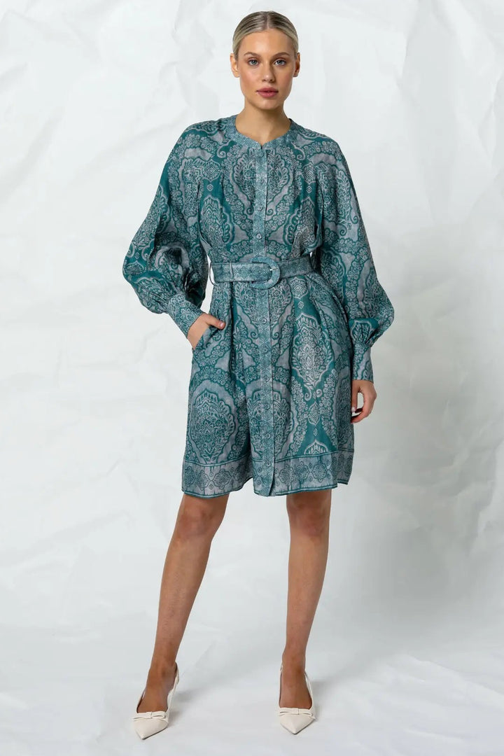 A model wearing a green mini dress with long puffed sleeves and an adjustable belt, featuring an intricate indigo henna design.