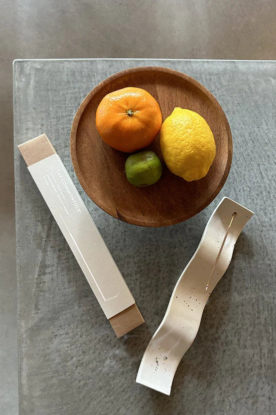 Two white ceramic items on a gray surface with a wooden bowl containing fruits.
