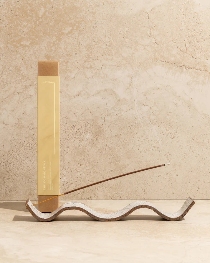 Incense stick holder with a lit incense stick on a beige stone background