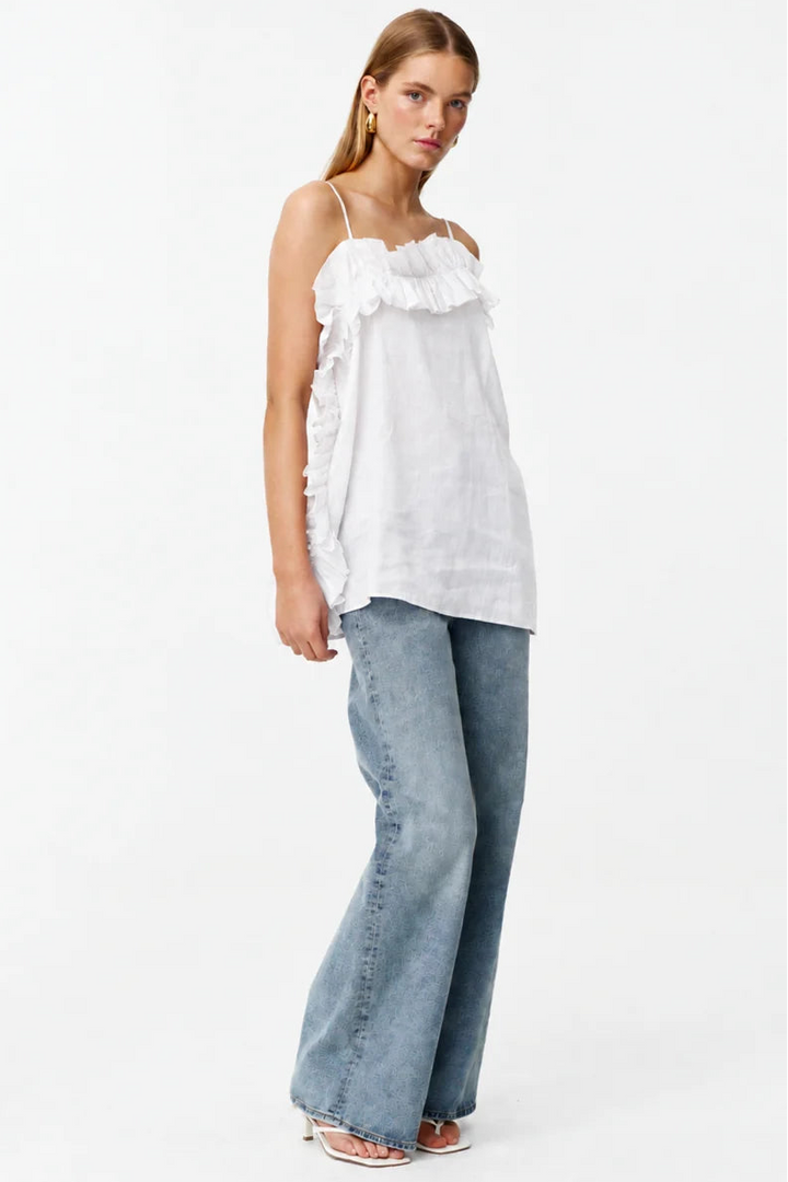 A woman modeling a white ruffled spaghetti-strap top and light-wash blue wide-leg jeans against a plain white studio background.