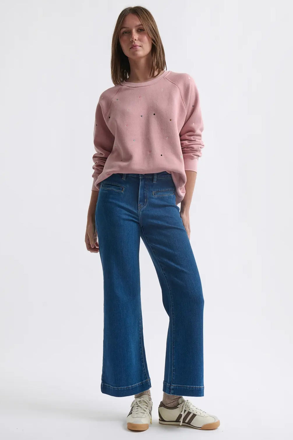 Woman wearing a pink sweater and blue jeans on a white background
