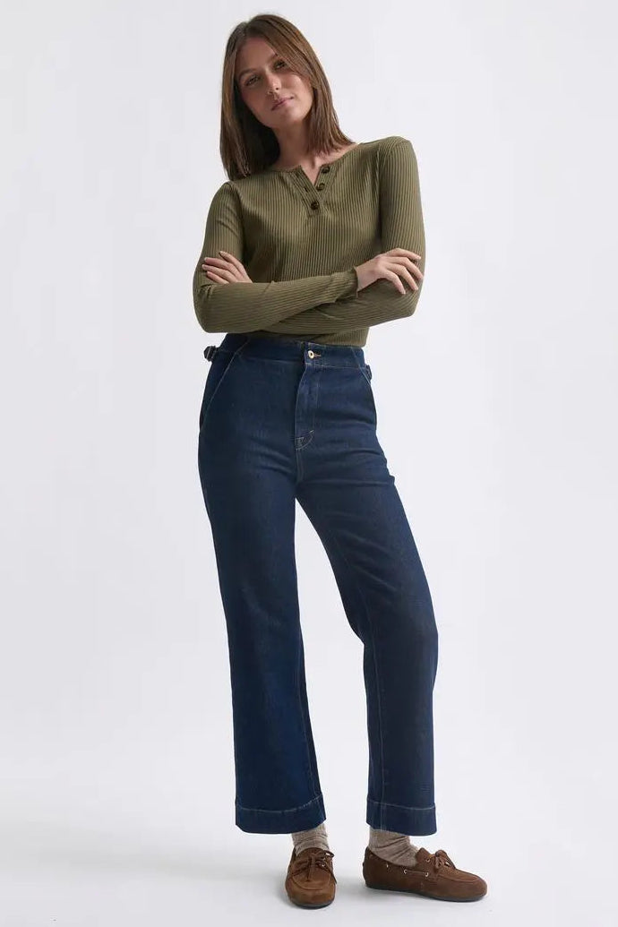 Woman wearing a green shirt and blue jeans standing against a white background