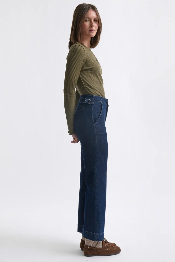 Woman wearing a green top and blue jeans standing against a white background
