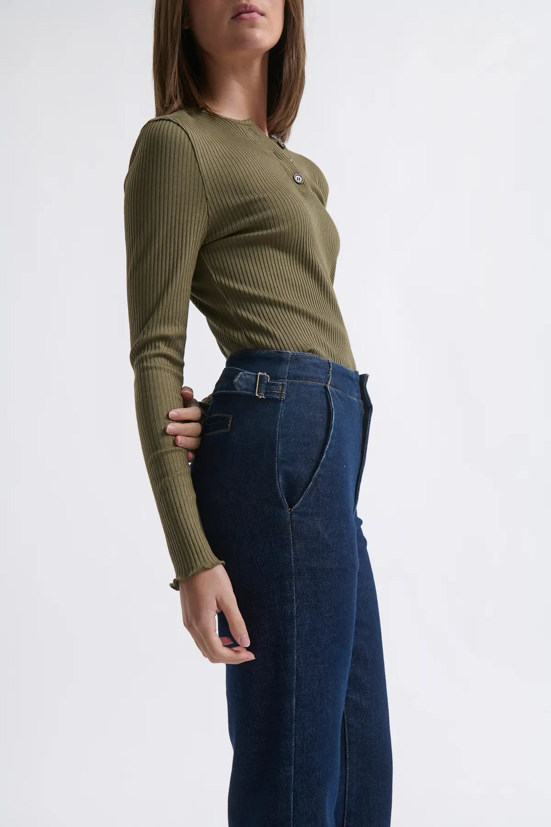 Person wearing a green ribbed sweater and blue jeans on a white background