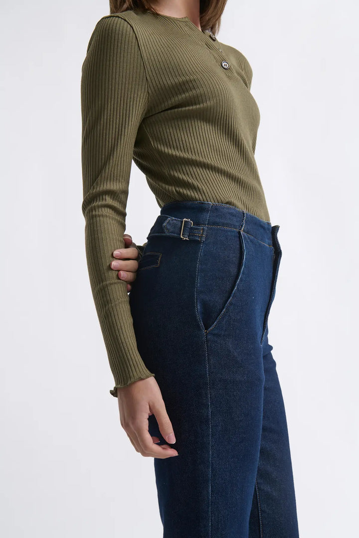 Person wearing a green ribbed sweater and blue jeans on a white background