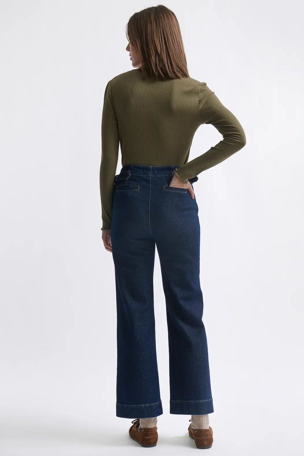 Person wearing a green long-sleeve top and blue jeans on a white background