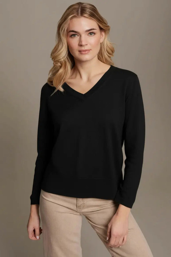 Woman wearing a black sweater and beige pants against a neutral background