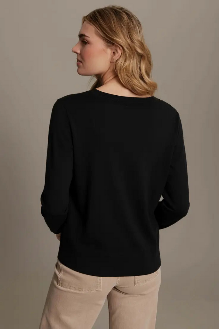 Woman wearing a black sweater and beige pants against a plain background