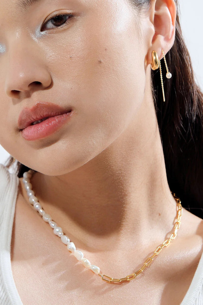 A person wearing a gold-colored baroque pearl necklace with a paperclip link chain design.