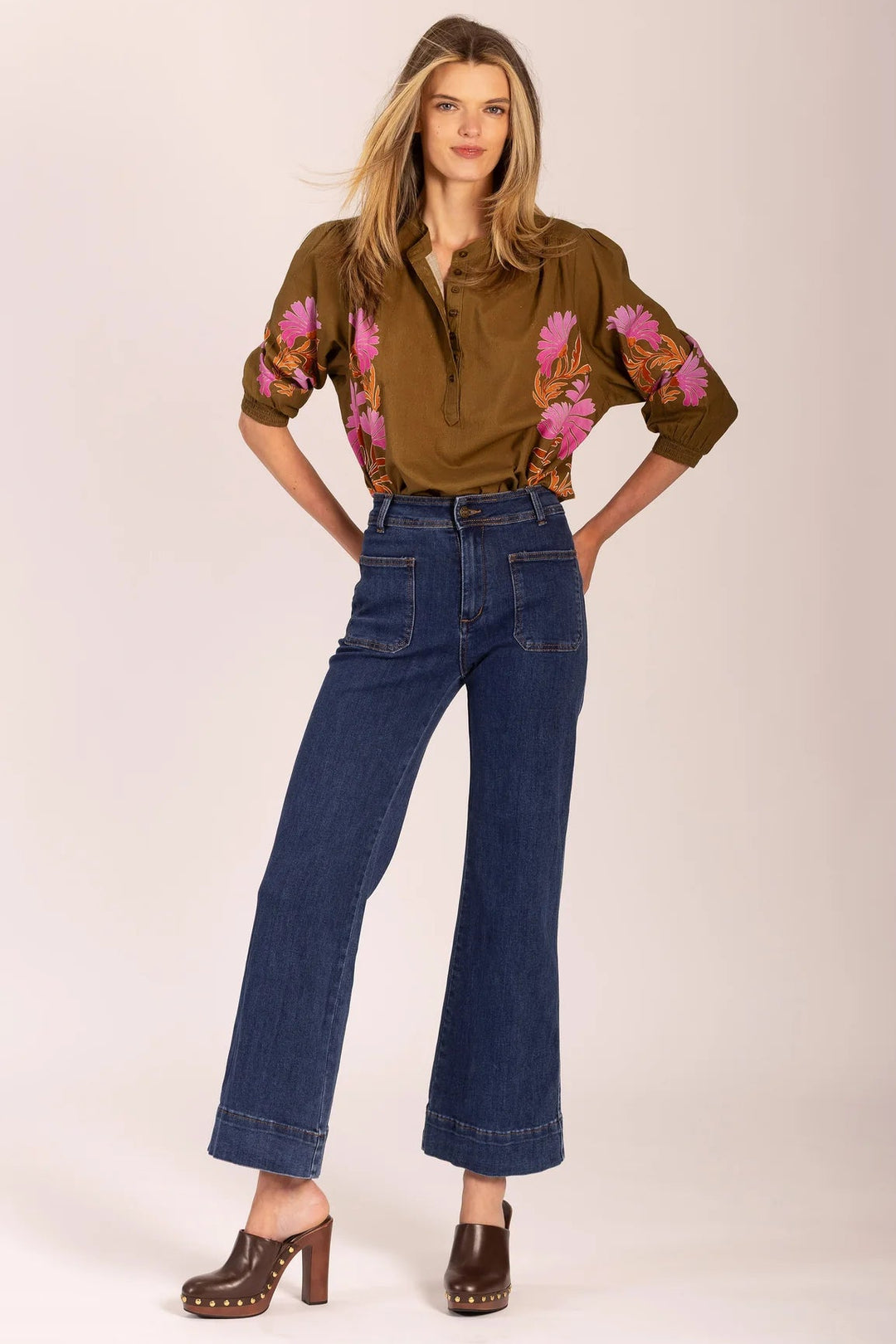 Woman wearing a brown floral blouse and blue jeans on a white background